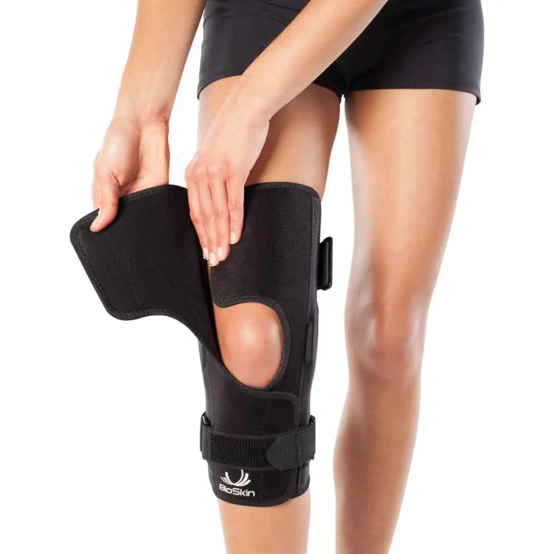 Das Bild zeigt die BioSkin Hinged Knee Sleeve Wraparound, eine stützende Kniebandage mit seitlichen Stäben zur Stabilisierung des Kniegelenks. Die Bandage besteht aus einem leichten, atmungsaktiven Material und ist so gestaltet, dass sie das Knie umschliesst und mit Klettverschlüssen individuell angepasst werden kann. 